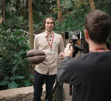 A man being filmed in the Rainforest Biome holding the Coco De Mer seed